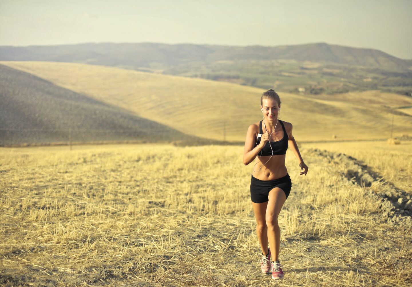 cheerful sportswoman running along hill in summer
